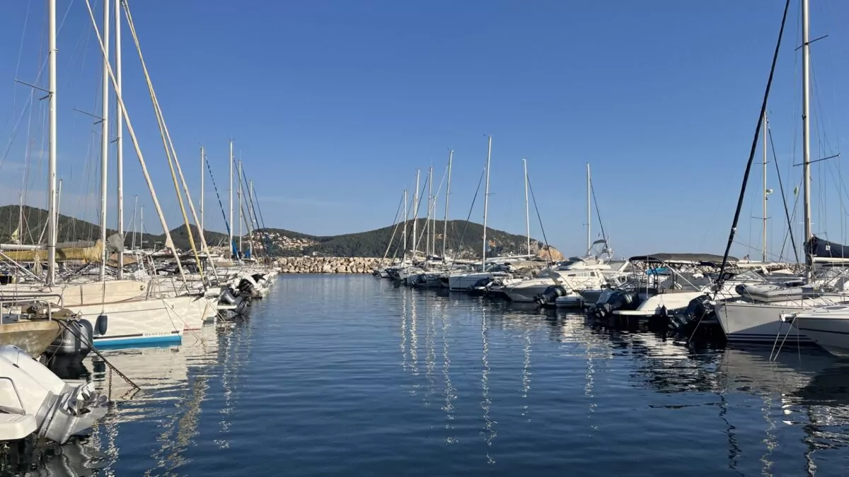 Port des Lecques avec des voiliers et des bateaux à moteur amarrés de part et d’autre du bassin, sur fond de collines verdoyantes et de ciel bleu ensoleillé.