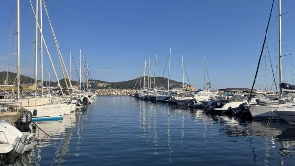 Port des Lecques avec des voiliers et des bateaux à moteur amarrés de part et d’autre du bassin, sur fond de collines verdoyantes et de ciel bleu ensoleillé.
