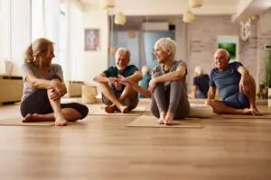 Quatre seniors, 2 femmes et 2 hommes, sont dans une salle de sport, assis au sol, sur des tapis de gym et discutent.