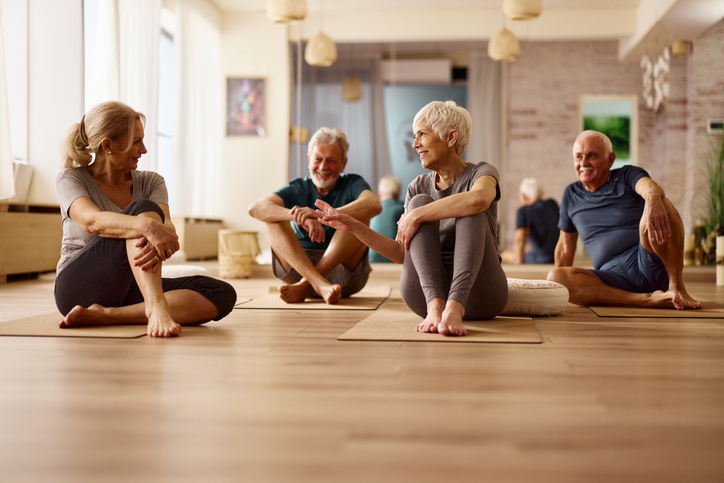 Quatre seniors, 2 femmes et 2 hommes, sont dans une salle de sport, assis au sol, sur des tapis de gym et discutent.