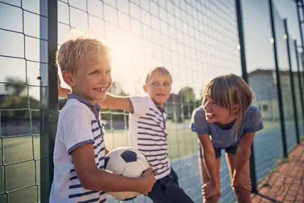 Trois enfants jouent au ballon en extérieur à proximité d'un stade