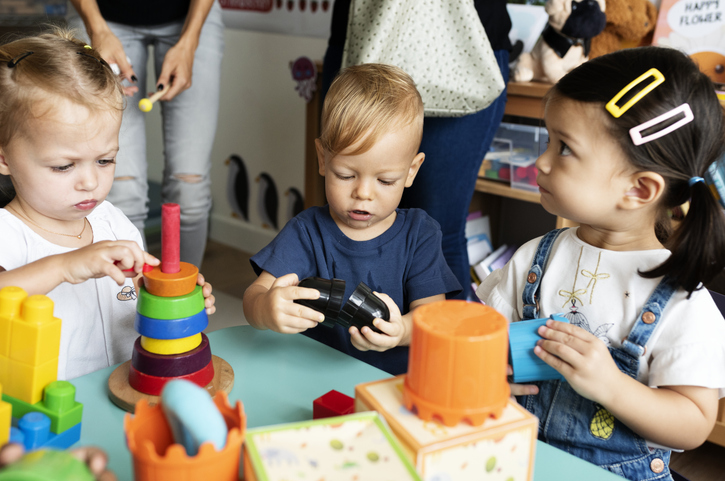 trois enfants en bas âge jouent autour d'une table à des jeux d'assemblage type lego