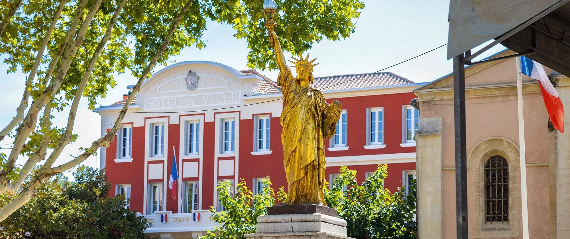 Au premier plan la Statue de la Liberté dorée de Saint-Cyr-sur-Mer et son Hôtel de Ville rouge en arrière plan