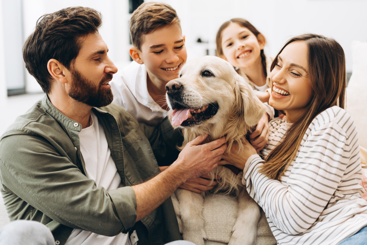Un gros plan sur une famille assise sur un canapé dans un salon composée d'un papa, d'une maman, de 2 enfants et d'un chien