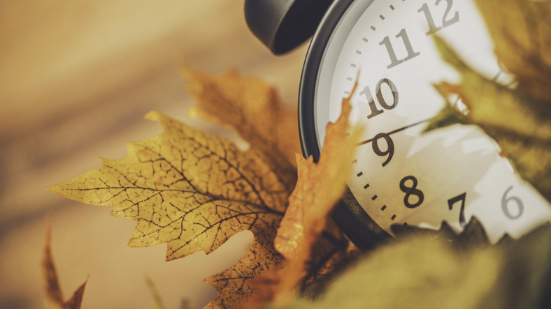 Réveil analogique posé sur des feuilles d’automne, illustrant le changement d’heure.