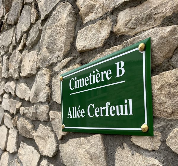 Panneau vert « Cimetière B – Allée Cerfeuil » fixé sur un mur en pierre.
