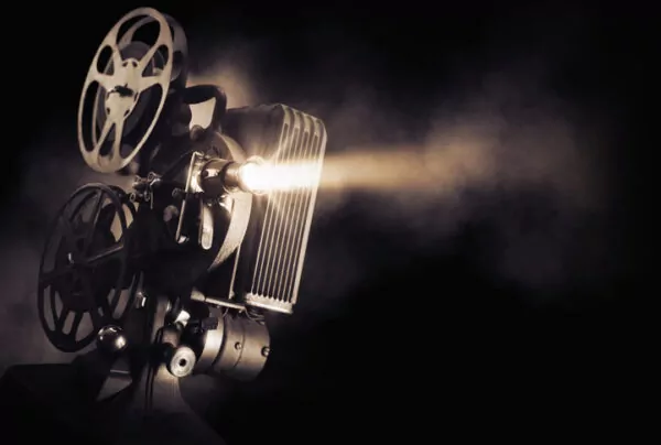 Ancien projecteur de cinéma diffusant un faisceau lumineux dans une pièce sombre, avec ses bobines de film visibles.