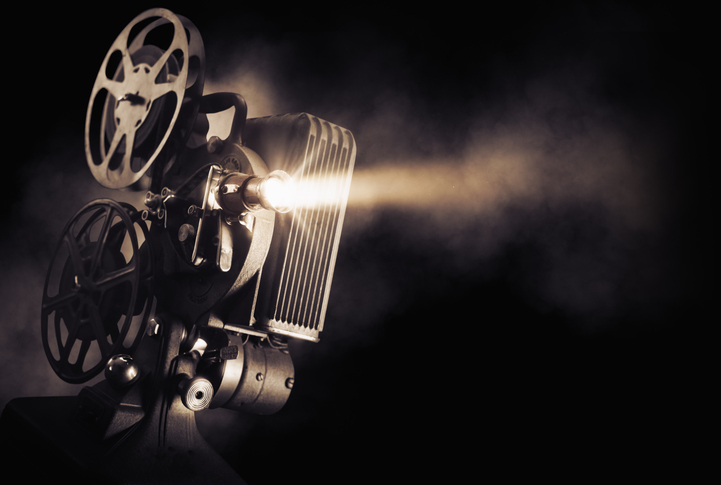 Ancien projecteur de cinéma diffusant un faisceau lumineux dans une pièce sombre, avec ses bobines de film visibles.