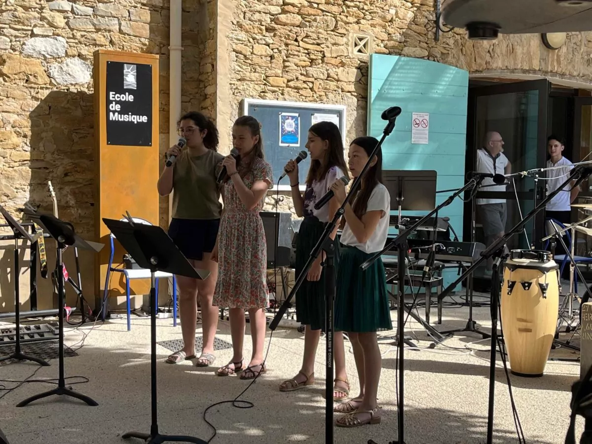 Quatre élèves de l’École municipale de musique de Saint-Cyr-sur-Mer chantent au micro lors d’un concert en plein air.