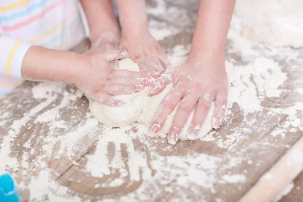 Des mains d’enfants pétrissent ensemble une pâte sur un plan de travail couvert de farine.