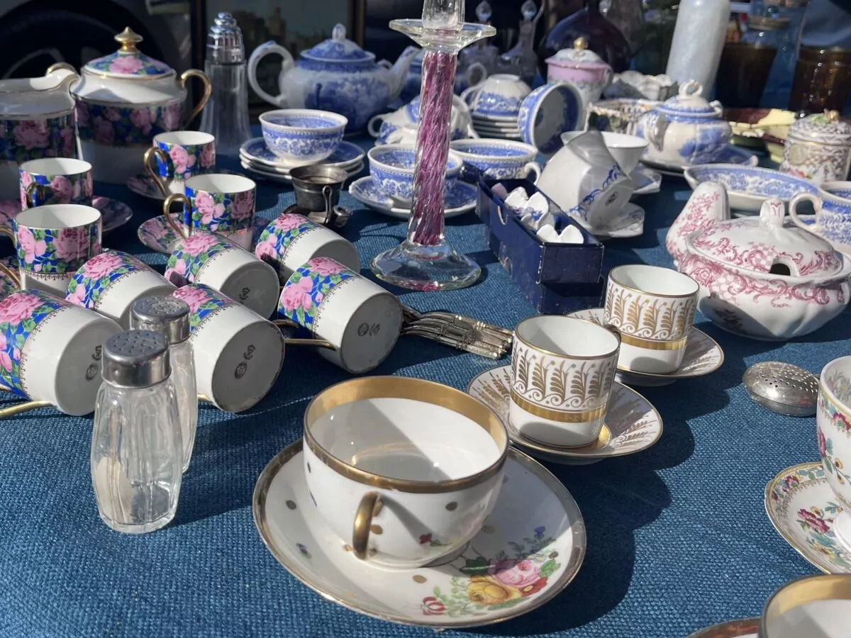 Stand de brocante présentant différentes pièces de vaisselle ancienne, notamment des tasses, soucoupes, théières et services en porcelaine aux motifs fleuris et colorés.