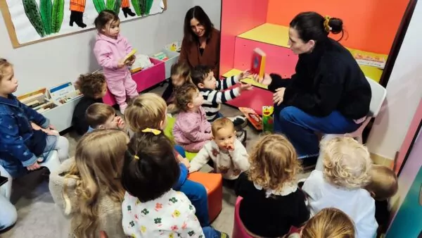 Un groupe d' enfants réunis autour d’une animatrice dans un espace de lecture coloré, lors d’une activité de découverte et de lecture de livre.