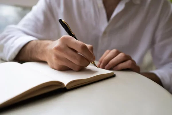 Personne qui ecrit au stylo dans un carnet ouvert sur une table