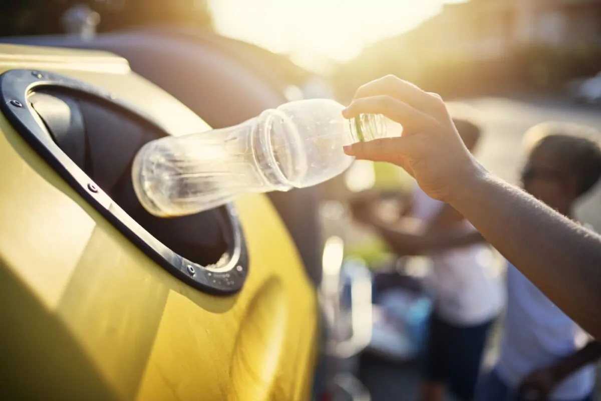 Main déposant une bouteille en plastique vide dans une poubelle de tri jaune.