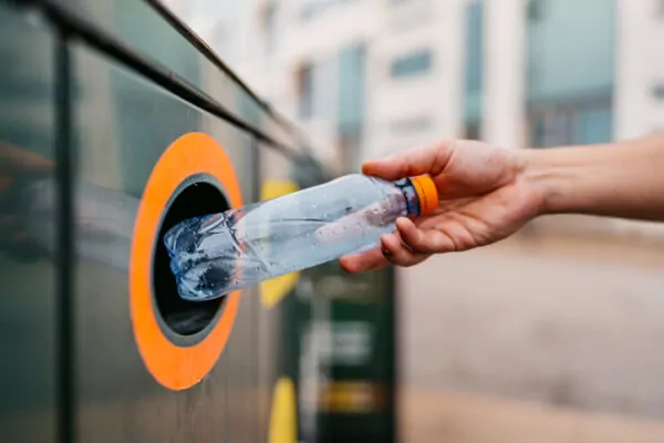 Focus sur une main en train de jeter une bouteille en plastique dans une poubelle de tri